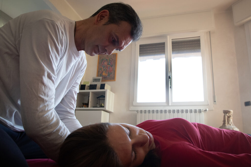 persona sdraiata su futon durante shiatsu, vestita, con operatore che lavora su spalle e collo