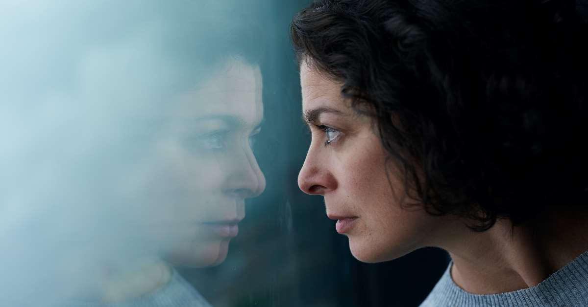 Donna che osserva il suo viso riflesso sul vetro - L'ansia è contagiosa?