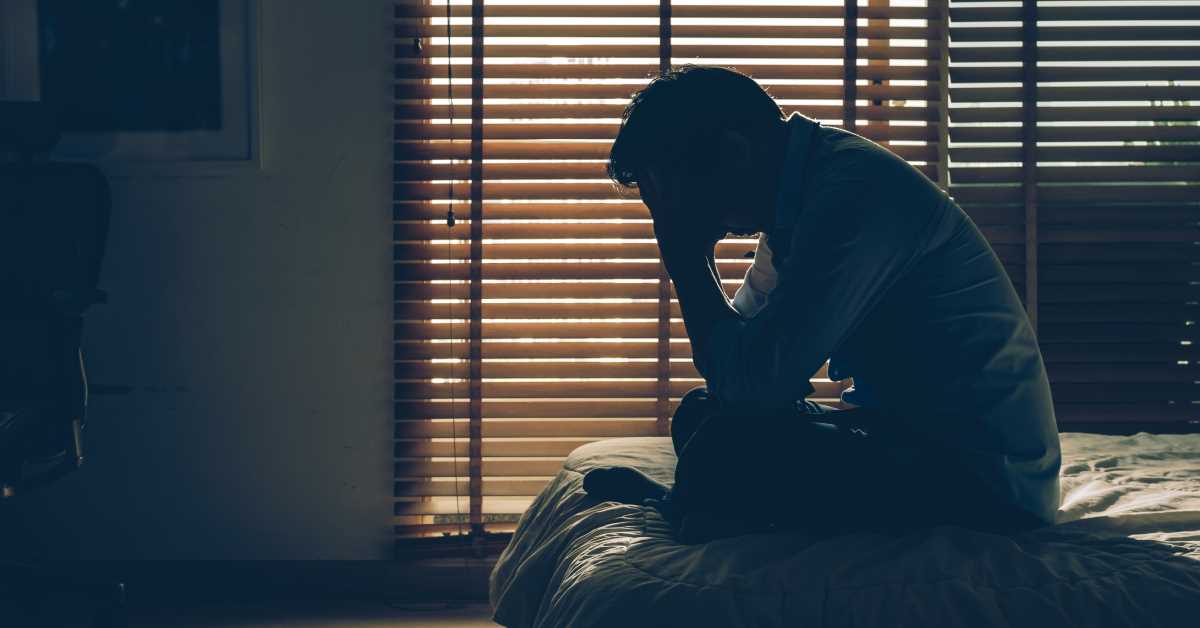 Mindfulness per chi soffre d’insonnia - Immagine di uomo preoccupato, seduto sul letto con la testa fra le mani.